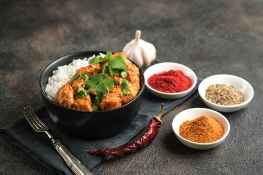 Geleneksel Asya baharatlı tavuk tikka masala pirinç domatesli ve siyah arka planda kişniş..