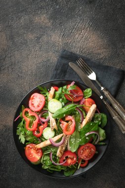 Taze sebze salatası, tavuk eti, otlar ve koyu bir tabakta zeytinyağı. Sağlıklı yiyecekler. Üst görünüm kopyalama alanı.