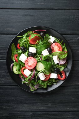 Feta, zeytin ve otlu taze sebze salatası koyu kırsal bir zeminde koyu bir tabakta. Sağlıklı vejetaryen yemeği. Üst görünüm kopyalama alanı.