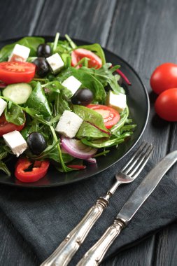 Feta, zeytin ve otlu taze sebze salatası koyu kırsal bir zeminde koyu bir tabakta. Sağlıklı vejetaryen yemekleri. 