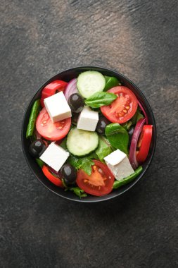 Feta, zeytin ve otlu taze sebze salatası koyu kırsal bir zeminde koyu bir tabakta. Sağlıklı vejetaryen yemeği. Üst görünüm kopyalama alanı.