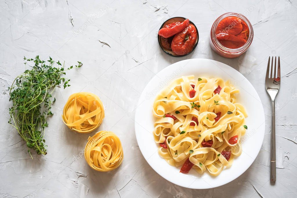 Italian traditional pasta tagliatelle with dried tomatoes and thyme on a light background.