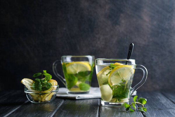 Fresh ginger tea with lemon slices, mint and honey on a dark background.