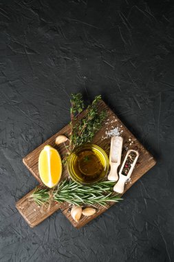 Selected ingredients for cooking. Lemon, herbs, olive oil and spices on a cutting board on a dark stone background.  Top view copy space.