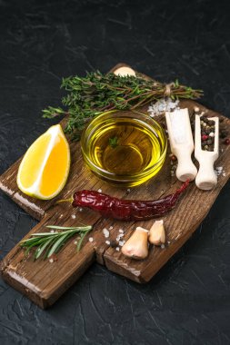 Selected ingredients for cooking. Lemon, herbs, olive oil and spices on a cutting board on a dark stone background.  Top view copy space.
