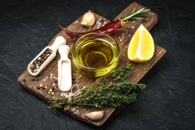 Selected ingredients for cooking. Lemon, herbs, olive oil and spices on a cutting board on a dark stone background.  Top view copy space.