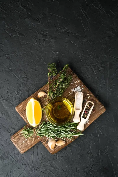 Selected ingredients for cooking. Lemon, herbs, olive oil and spices on a cutting board on a dark stone background.  Top view copy space.