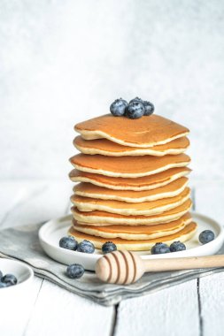 Pancakes with berries and honey on a light rustic background copy space. Very hearty tasty breakfast.
