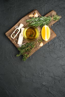 Selected ingredients for cooking. Lemon, herbs, olive oil and spices on a cutting board on a dark stone background.  Top view copy space.