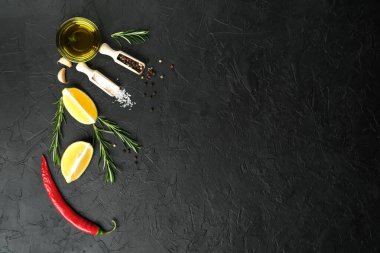 Selected ingredients for cooking. Lemon, herbs, olive oil and spices on a cutting board on a dark stone background.  Top view copy space.
