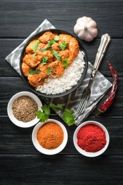 Geleneksel Asya baharatlı tavuk tikka masala pirinç domatesli ve siyah arka planda kişniş..