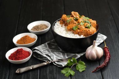 Geleneksel Asya baharatlı tavuk tikka masala pirinç domatesli ve siyah arka planda kişniş..