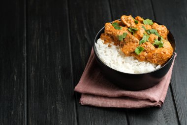 Geleneksel Asya baharatlı tavuk tikka masala pirinç domatesli ve siyah arka planda kişniş..