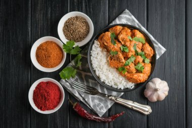 Geleneksel Asya baharatlı tavuk tikka masala pirinç domatesli ve siyah arka planda kişniş..