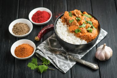 Geleneksel Asya baharatlı tavuk tikka masala pirinç domatesli ve siyah arka planda kişniş..