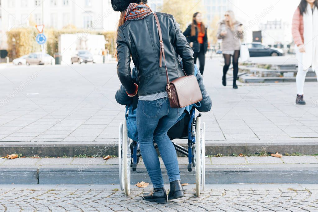 rear view of a woman helping a disabled person to go down the steps with the wheelchair - architectural boundaries in the cities concept