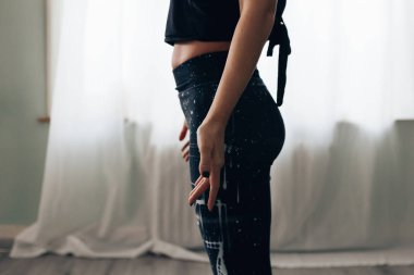 Orta vücut ve pencerenin önünde yoga yapan spor kıyafetli bir kadının açık el görüntüsü.