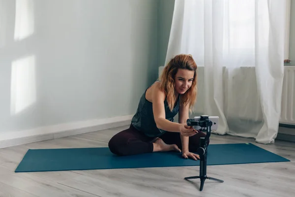 Jeune femme assise sur un tapis en tenue de sport qui commence à s'enregistrer avec un téléphone portable sur un trépied à cardan - concept de star des médias sociaux — Photo