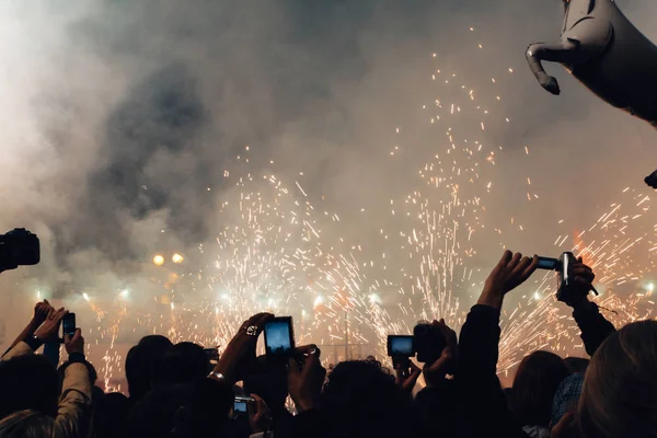 people with raised arms recording with phones and cameras at outdoors public event by night