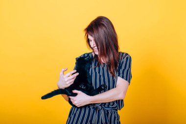 Bir kadın kollarında siyah bir kedi tutuyor. Birbirlerinin gözlerinin içine bakıp eğleniyorlar.