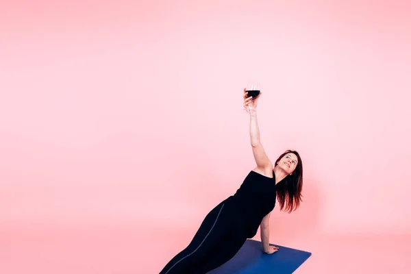Yoga yaparken elinde bir kadeh kırmızı şarap tutan genç bir kadın - şarap ve yoga trend konsepti 