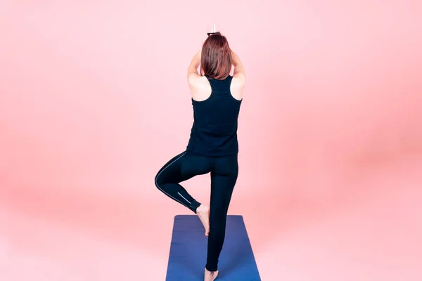 Arka planda, Asya yogası yapan genç bir kadının pembe arka planda bir bardak kırmızı şarap tutuşu yeni moda şarap ve yoga konsepti.