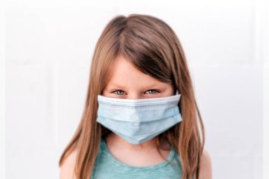 Mavi gözlü bir kızın portresi anti-virüs maskesi takıyor ve kendine güveni yüksek pozitiflikle kameraya bakıyor.