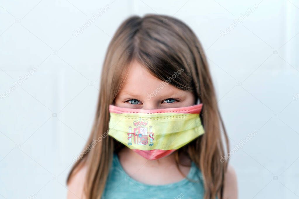 portrait of a girl with blue eyes and intense assertive positive gaze looking straight to the camera wearing an anti-virus mask with the spanish flag colors