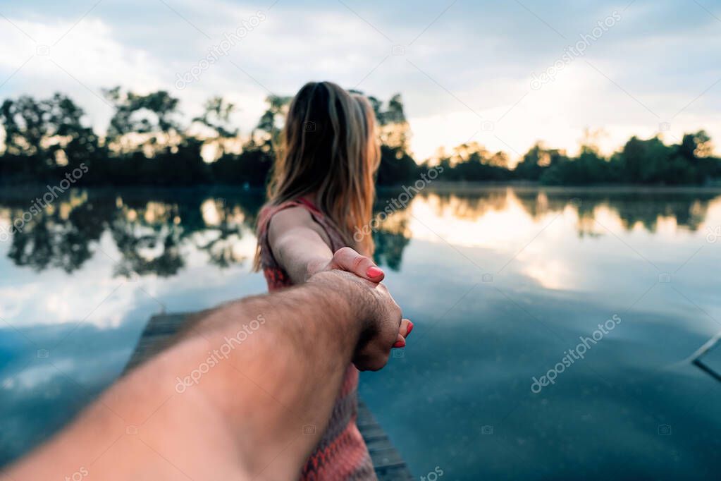 view of a woman from behind walking and watching the water of the lake at sunset holding the hand of a man