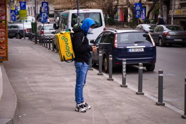Bükreş, Romanya - 22 Mart 2020: Maske takan bir Glovo gıda kuryesi. Romanya 'da restoranlar kapalı ve sadece koronavirüs nedeniyle olağanüstü hal sırasında teslimatlara izin veriliyor.