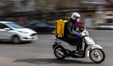 Bükreş, Romanya - 26 Mart 2020: Mobilette maske takan Glovo gıda dağıtım kuryesi. Restoranlar kapalıdır ve sadece acil durumlarda Coronavirus nedeniyle teslimatlara izin verilir.