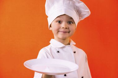 hamur için bir tabak turuncu bir arka plan üzerinde tutarak komik çocuk şef aşçı