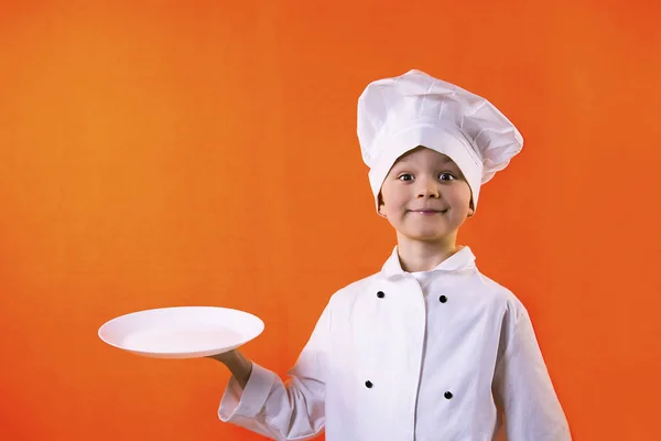 Zabawny Chłopak Kucharz Trzyma Talerz Ciasta Pomarańczowym Tle — Zdjęcie stockowe