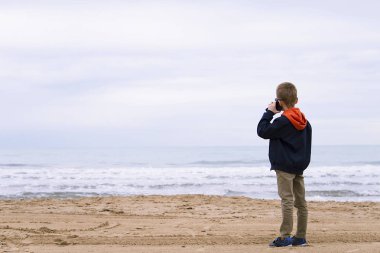 oğlan baharda deniz kıyısı, telefonda konuşuyor