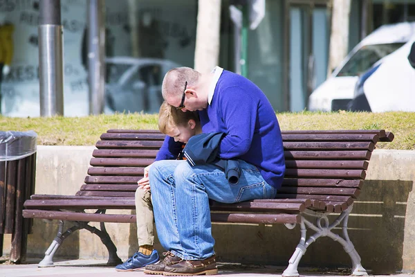 father calms an upset son on a bench in the city in the spring