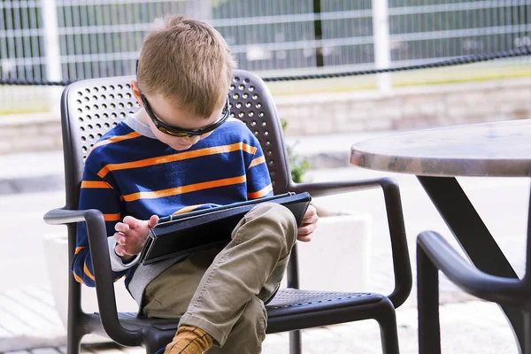boy playing a tablet in a street cafe in the spring