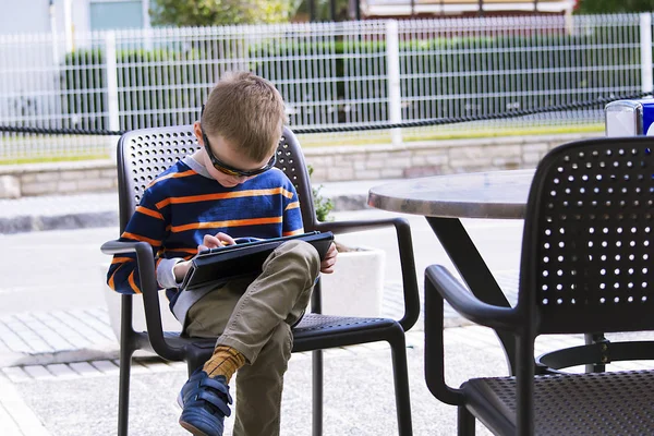 boy playing a tablet in a street cafe in the spring