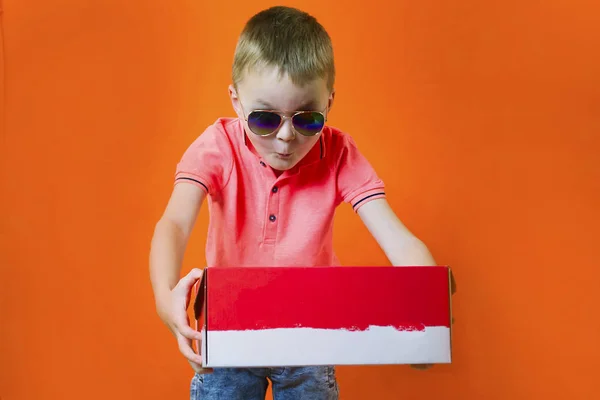 滑稽的男孩拿着一个盒子在明亮的橙色背景 — 图库照片
