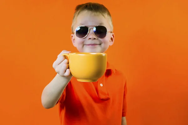 Vicces Fiú Tart Egy Nagy Csésze Világos Narancsszínű Háttérrel — Stock Fotó