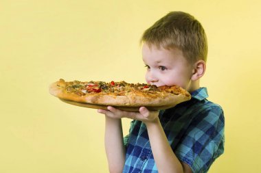parlak sarı bir arka plan üzerinde büyük bir pizza yeme komik çocuk
