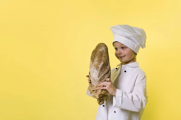 明るい黄色の背景でパンを持って面白い少年シェフ シェフ — ストック写真