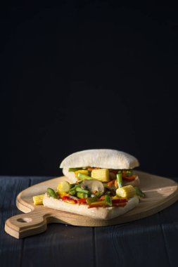 Soslu kızarmış sebzeli sandviç ve siyah ahşap arka planda mantar.