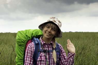 Yürüyüş gezisinde sırt çantalı güzel bir kadın neşeli bir ruh hali içinde çayırları geçiyor..