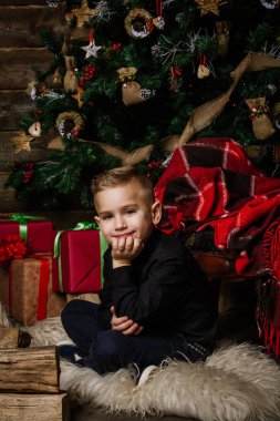 Çok iyi bir çocuk oturur yakınındaki bir Noel ağacı gülümseyerek mutlu bir şekilde sarılmış