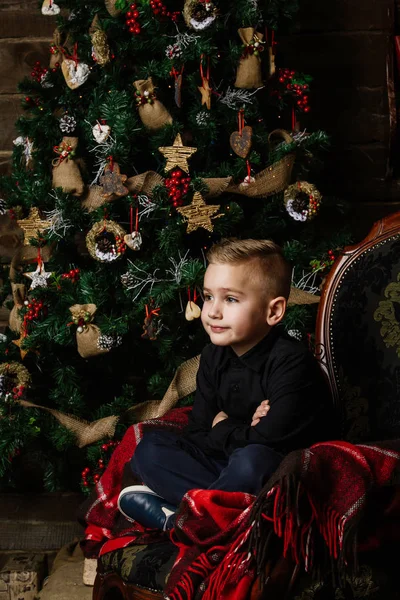 Muy buen chico se sienta cerca de un árbol de Navidad sonriendo felizmente envuelto — Foto de Stock