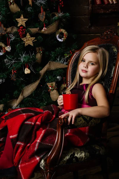 Molto bella ragazza seduta su una sedia vicino a un albero di Natale smi — Foto Stock