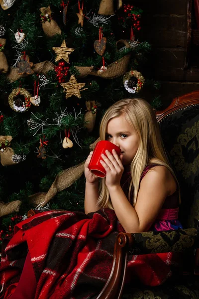 Menina muito bonita sentada em uma cadeira perto de uma árvore de Natal smi — Fotografia de Stock