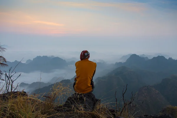 Mann sitzt auf steinerner Spitze eines hohen Berges — Stockfoto