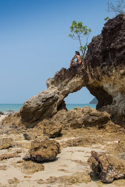 Sexy male vagabond beach bum taking on a rock — Stock Photo, Image