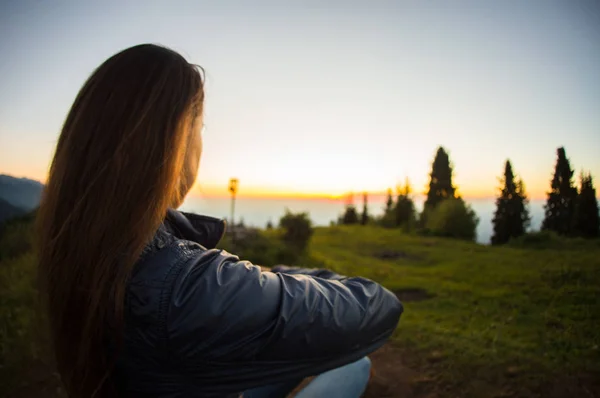 Young woman sitting on a rock with backpack and looking to the horizon — Stock Photo, Image